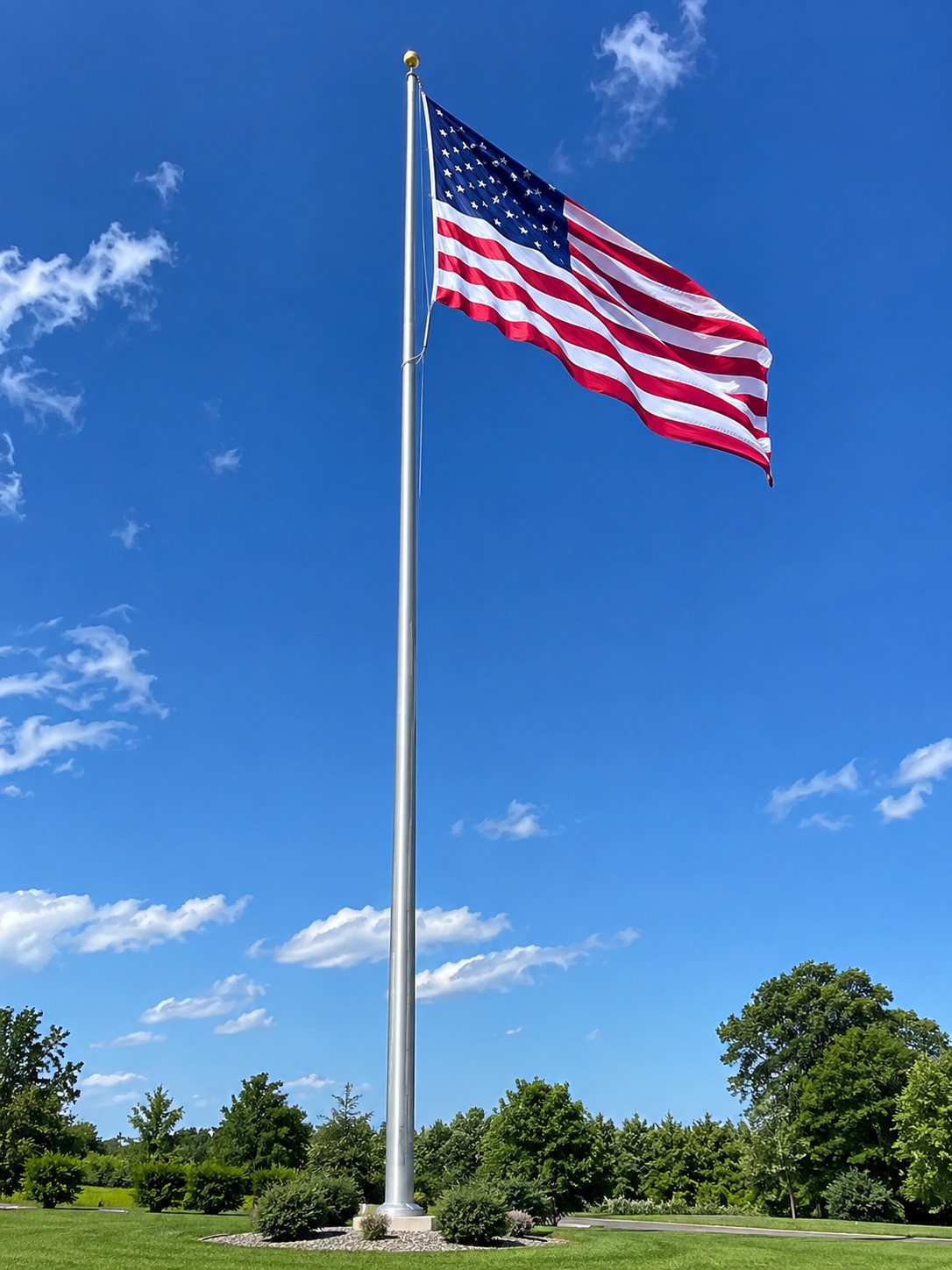 An American flag flying from a tall silver flagpole against a blue sky